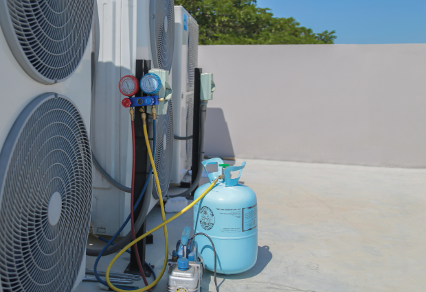 Air conditioning service technician using gauges to check refrigerant and add refrigerant.