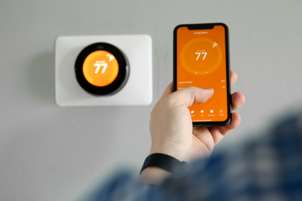 A Man uses a mobile phone with a smart home thermostat app in a modern living room.