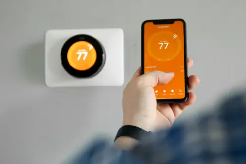 A Man uses a mobile phone with a smart home thermostat app in a modern living room.